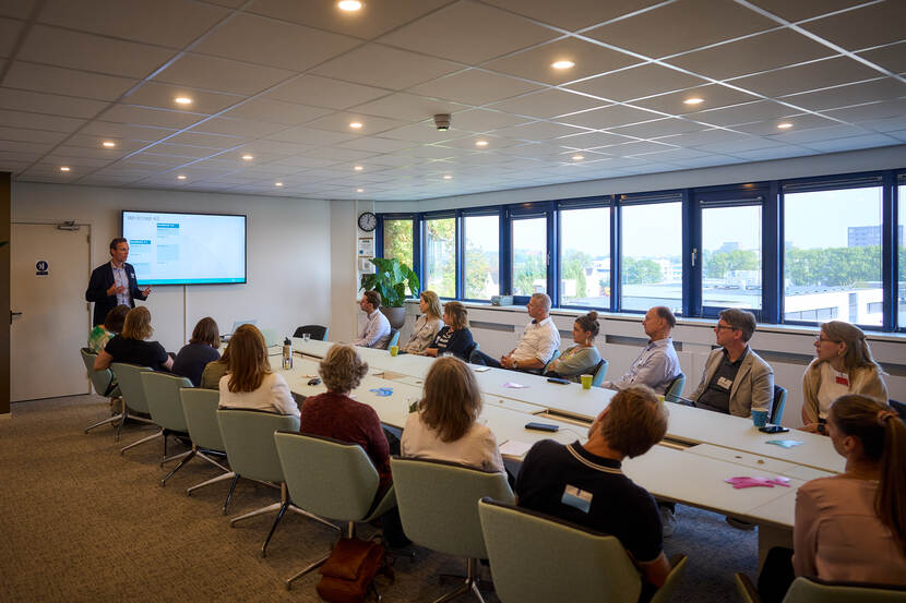 Mensen aan een langwerpige tafel luisteren naar een spreker