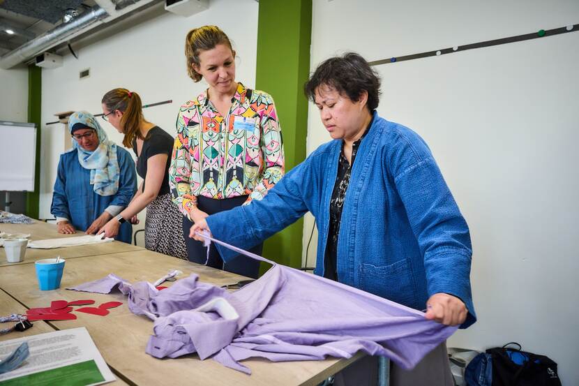 Vier mensen staan bij tafels waar ze met kleding bezig zijn