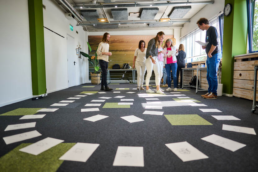 Er liggen allemaal A4-tjes op de grond waarmee een groep mensen een spel speelt